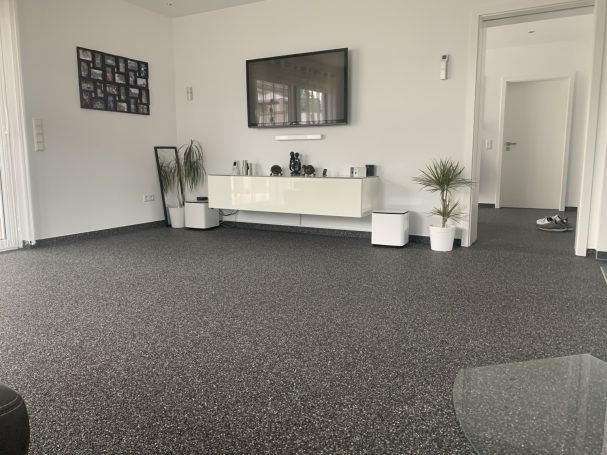 Dunkler Steinteppich im Wohnzimmer mit weißem Sideboard, Pflanzen und offenem Übergang zum Flur.